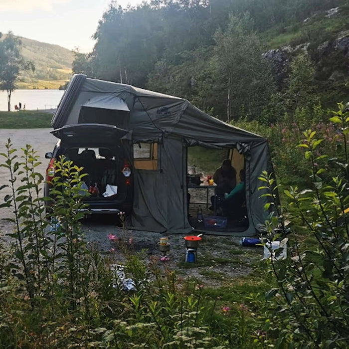 Voiture avec une tente de toit installée en pleine nature, montrant un camping confortable pour 2-3 personnes près d'un lac et des montagnes.