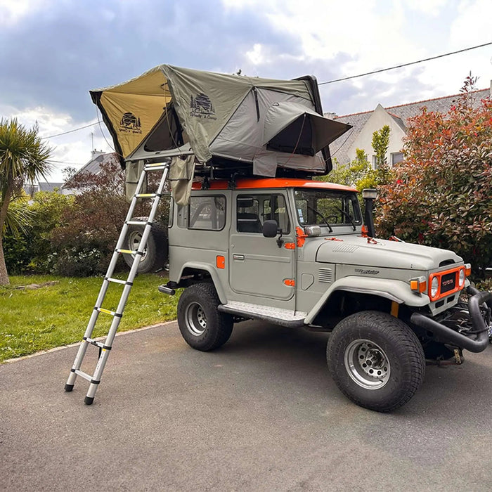 Véhicule 4x4 avec tente de toit rigide pour 2-3 personnes, idéal pour des aventures de camping en plein air, échelle attachée, garé dans une allée.
